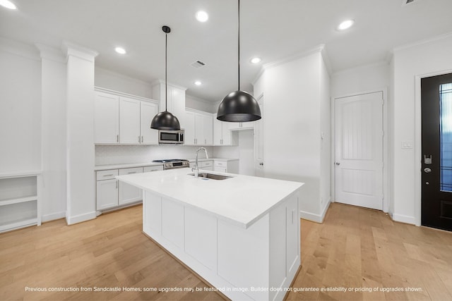 kitchen featuring sink, hanging light fixtures, stainless steel appliances, light hardwood / wood-style floors, and white cabinets