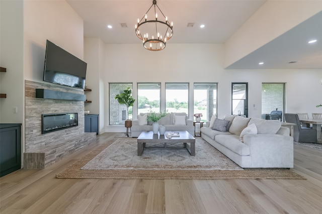 living room with a notable chandelier, a stone fireplace, light wood-type flooring, and a high ceiling