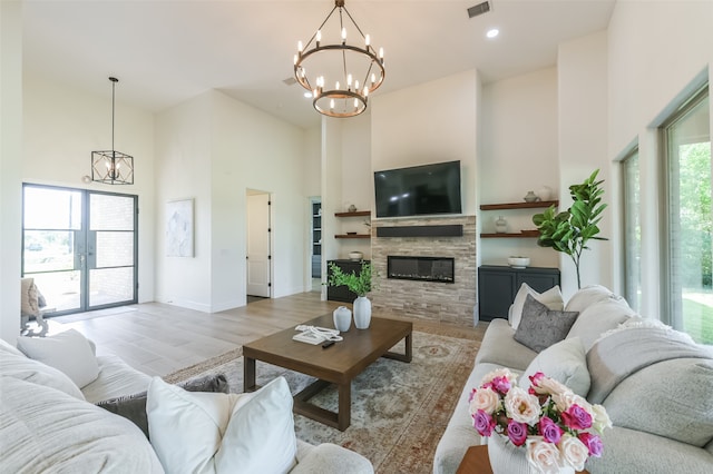 living room featuring a high ceiling, light hardwood / wood-style floors, a stone fireplace, and a notable chandelier