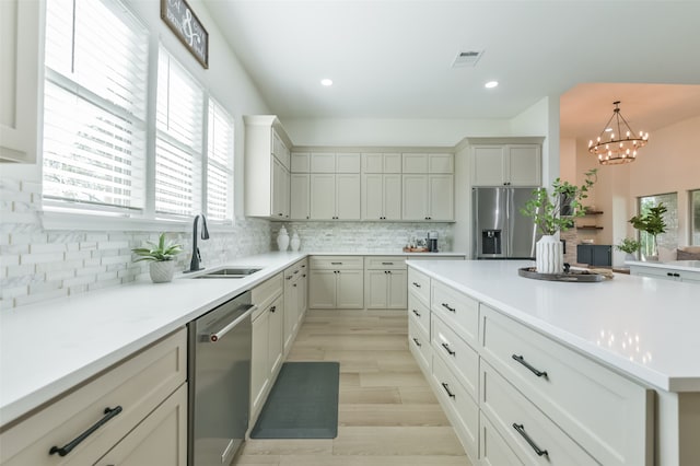 kitchen featuring appliances with stainless steel finishes, light wood-type flooring, hanging light fixtures, and a healthy amount of sunlight