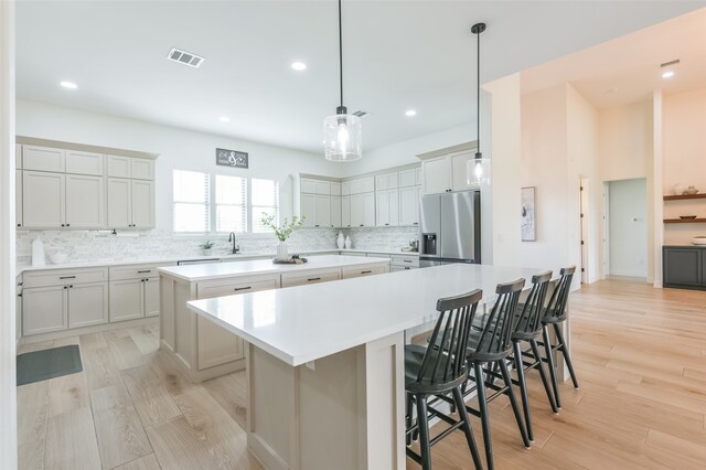 kitchen with light hardwood / wood-style flooring, stainless steel refrigerator with ice dispenser, pendant lighting, a breakfast bar, and a kitchen island