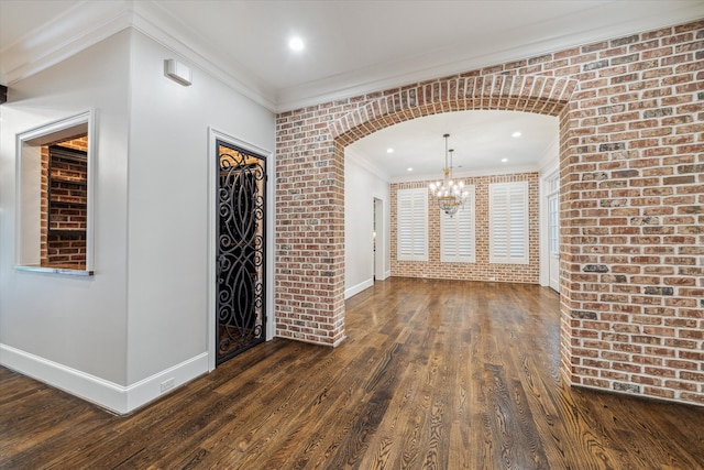 interior space featuring dark hardwood / wood-style flooring, ornamental molding, brick wall, and an inviting chandelier