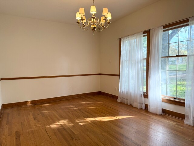 empty room with a wealth of natural light, wood-type flooring, and a notable chandelier