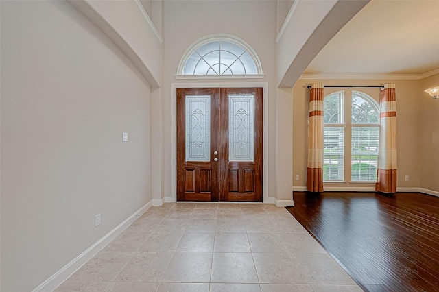 foyer entrance featuring ornamental molding, a towering ceiling, and light hardwood / wood-style flooring