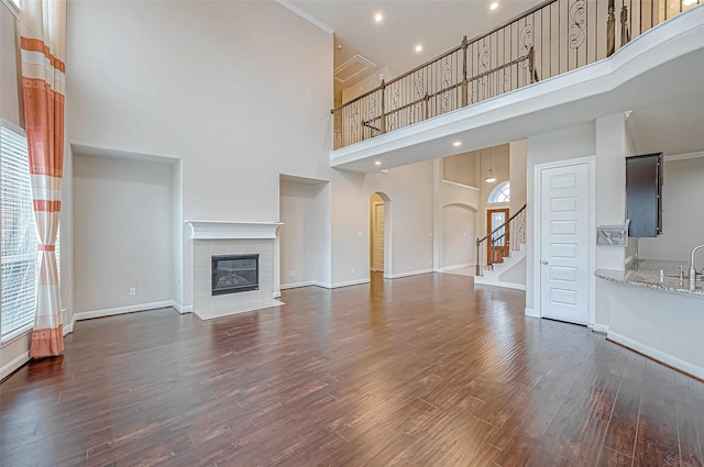 unfurnished living room featuring sink, dark hardwood / wood-style floors, a towering ceiling, a tiled fireplace, and ornamental molding