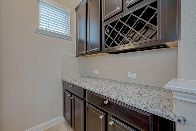 kitchen featuring dark brown cabinets, light stone counters, and backsplash