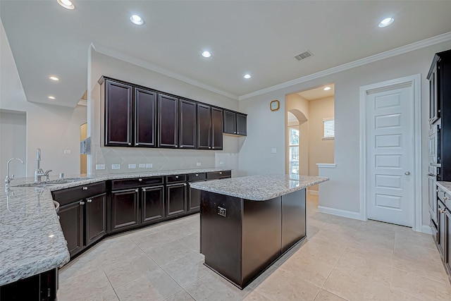 kitchen featuring dark brown cabinetry, crown molding, light tile patterned floors, and light stone counters