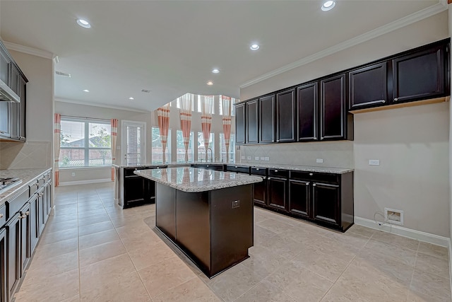 kitchen featuring backsplash, sink, crown molding, a kitchen island, and light stone counters