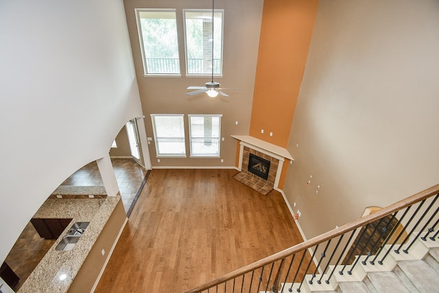 unfurnished living room with ceiling fan, a fireplace, a high ceiling, and light wood-type flooring