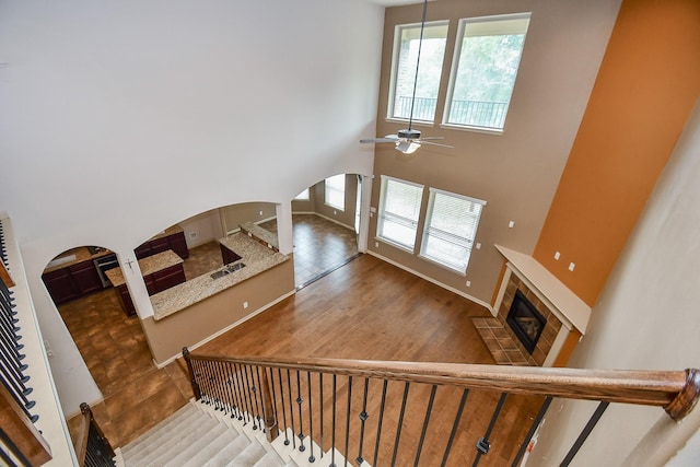 stairs featuring a tile fireplace, a high ceiling, ceiling fan, and wood-type flooring