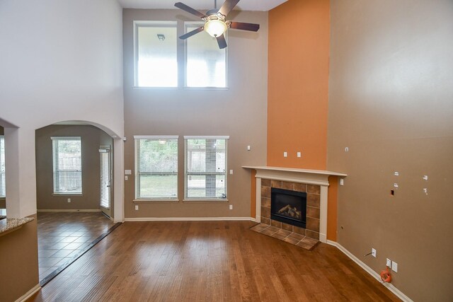 unfurnished living room featuring a tile fireplace, hardwood / wood-style floors, a towering ceiling, and ceiling fan