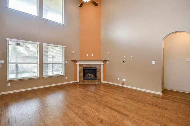 unfurnished living room with a fireplace, ceiling fan, light hardwood / wood-style flooring, and a high ceiling