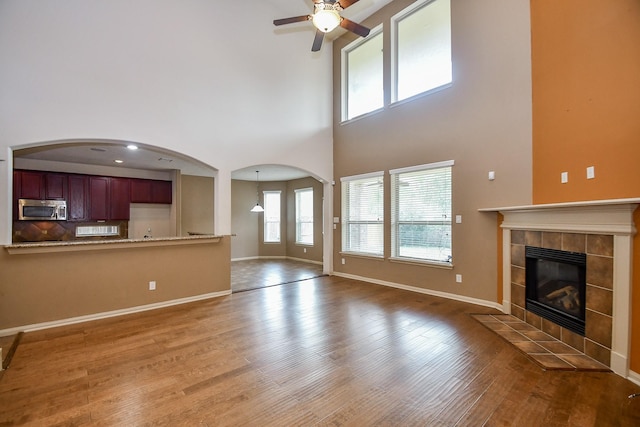 unfurnished living room featuring a tile fireplace, ceiling fan, hardwood / wood-style floors, and a towering ceiling