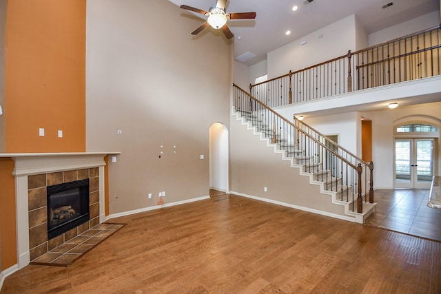 unfurnished living room featuring a tile fireplace, ceiling fan, a towering ceiling, and hardwood / wood-style flooring