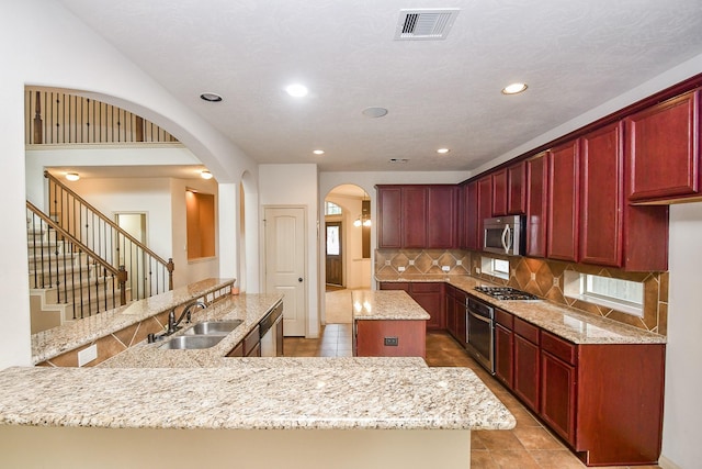 kitchen with a center island, sink, decorative backsplash, light stone counters, and stainless steel appliances