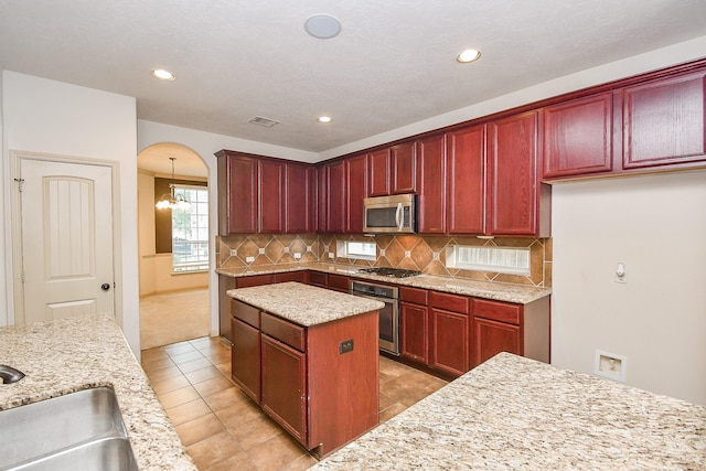 kitchen with stainless steel appliances, tasteful backsplash, light stone counters, decorative light fixtures, and a kitchen island