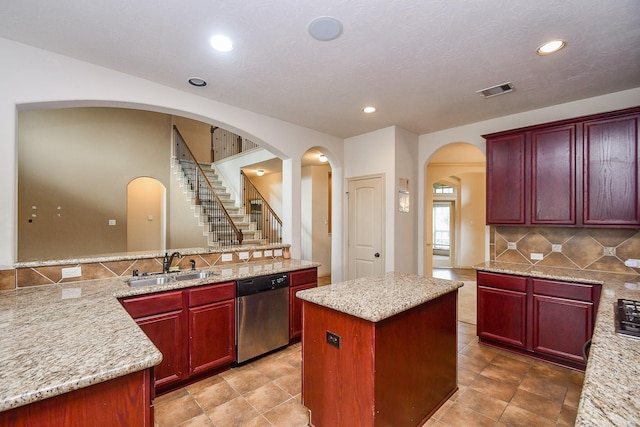 kitchen with dishwasher, sink, light stone counters, decorative backsplash, and a kitchen island