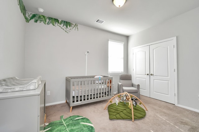 bedroom featuring a crib, light carpet, and a closet