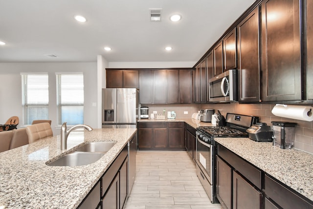 kitchen featuring appliances with stainless steel finishes, light stone counters, dark brown cabinets, and sink