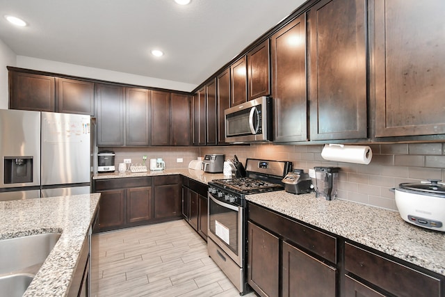 kitchen with light stone counters, dark brown cabinetry, backsplash, and appliances with stainless steel finishes