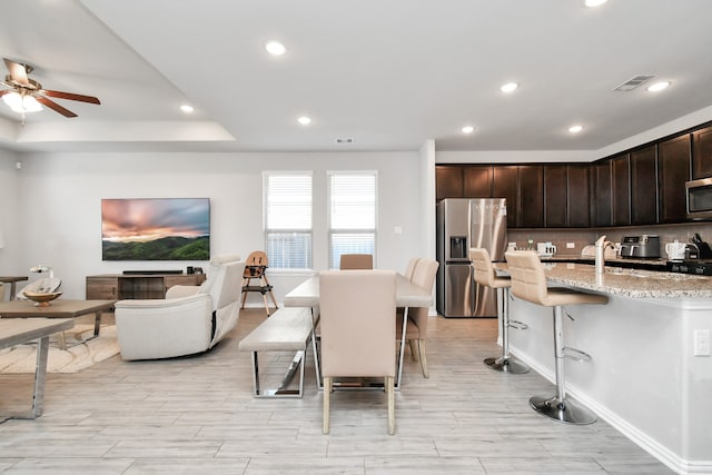 kitchen featuring dark brown cabinetry, ceiling fan, stainless steel appliances, light stone counters, and a breakfast bar area