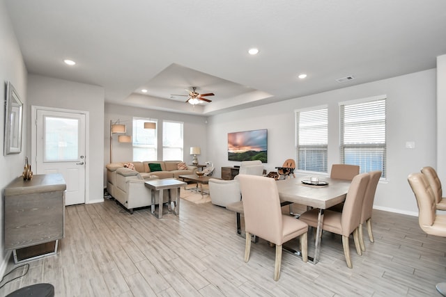 dining space featuring ceiling fan, a raised ceiling, and light wood-type flooring