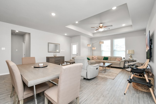 dining area featuring ceiling fan, light wood-type flooring, and a tray ceiling