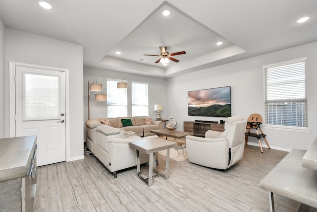 living room featuring light wood-type flooring, a tray ceiling, and ceiling fan