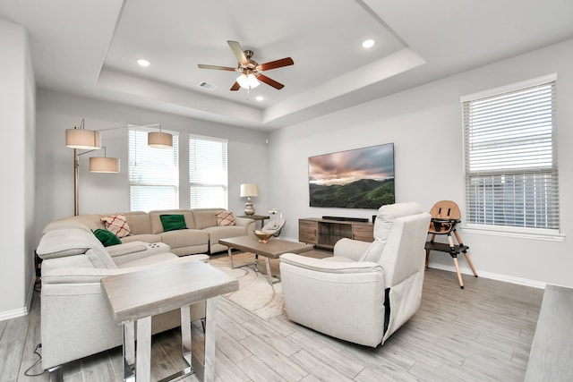 living room featuring a raised ceiling, a wealth of natural light, ceiling fan, and light hardwood / wood-style floors