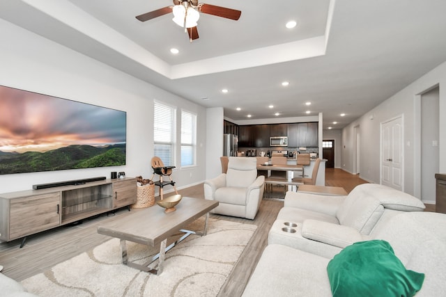 living room with a raised ceiling, ceiling fan, and light hardwood / wood-style floors