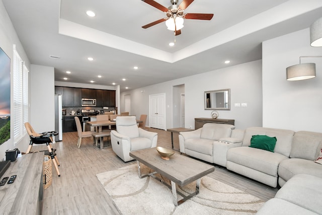 living room featuring a tray ceiling, ceiling fan, and light wood-type flooring