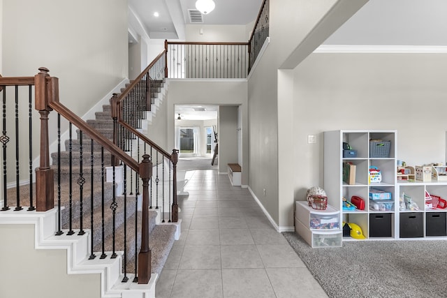 foyer entrance featuring light tile patterned flooring, crown molding, and a high ceiling