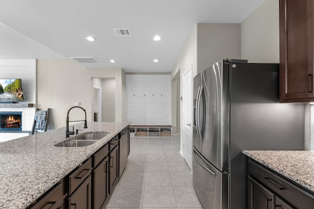 kitchen with light stone countertops, stainless steel fridge, dark brown cabinetry, sink, and light tile patterned flooring