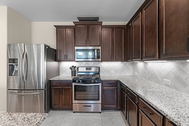 kitchen featuring decorative backsplash, light stone counters, light tile patterned floors, and stainless steel appliances