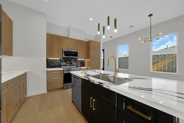 kitchen featuring sink, light stone counters, a chandelier, light hardwood / wood-style floors, and appliances with stainless steel finishes