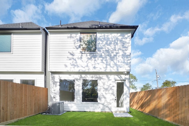 rear view of house featuring central air condition unit and a lawn