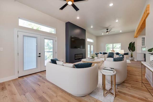 living room featuring a large fireplace, ceiling fan, light hardwood / wood-style flooring, and french doors