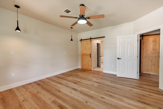 unfurnished bedroom with ceiling fan, a barn door, and light wood-type flooring