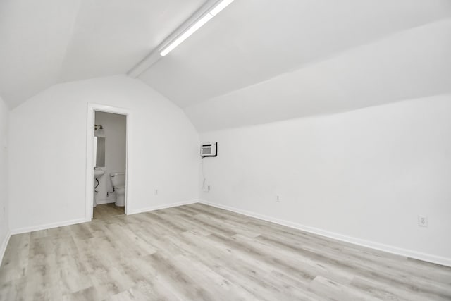 additional living space with vaulted ceiling with beams, an AC wall unit, and light hardwood / wood-style flooring