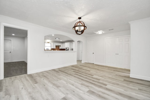 unfurnished living room featuring light wood-type flooring, an inviting chandelier, and crown molding