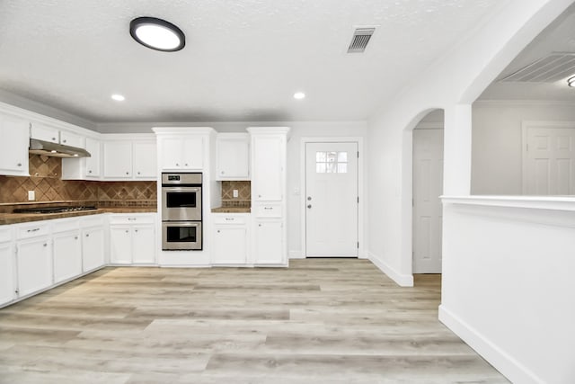 kitchen with white cabinets, appliances with stainless steel finishes, light wood-type flooring, and tasteful backsplash