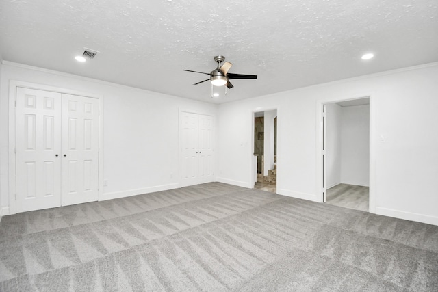 unfurnished bedroom featuring light carpet, two closets, ensuite bath, and ceiling fan