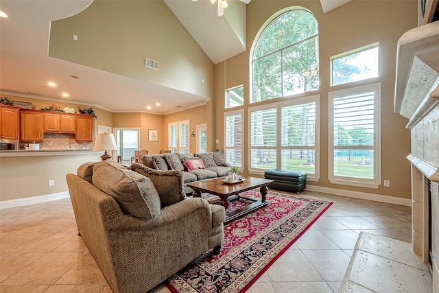 tiled living room featuring a towering ceiling, plenty of natural light, ornamental molding, and a tiled fireplace