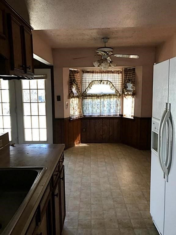 kitchen featuring ceiling fan, white fridge with ice dispenser, wood walls, and dark brown cabinets