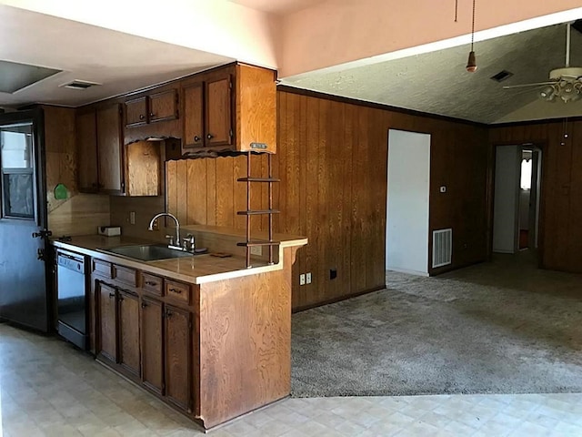 kitchen with wood walls, sink, black dishwasher, light colored carpet, and kitchen peninsula