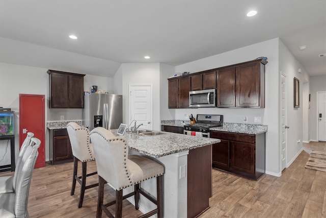 kitchen featuring appliances with stainless steel finishes, a kitchen island with sink, light wood-type flooring, a kitchen breakfast bar, and sink