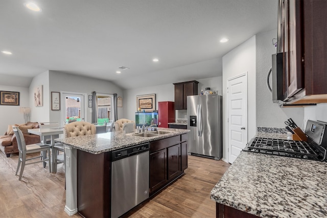 kitchen with an island with sink, appliances with stainless steel finishes, lofted ceiling, light stone countertops, and sink