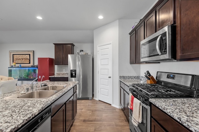 kitchen featuring sink, dark brown cabinetry, light wood-type flooring, appliances with stainless steel finishes, and light stone counters