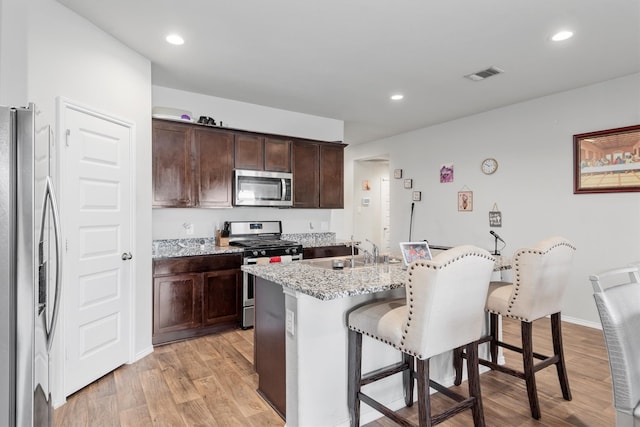 kitchen featuring stainless steel appliances, a kitchen island with sink, a kitchen breakfast bar, light stone countertops, and sink