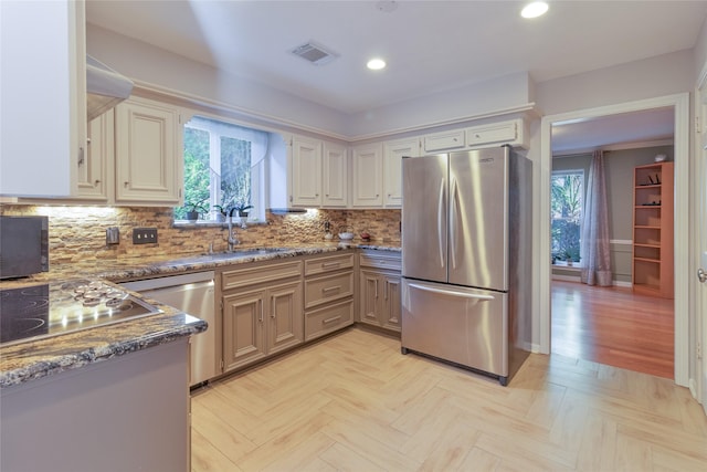 kitchen with sink, dark stone countertops, backsplash, light parquet floors, and stainless steel appliances